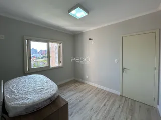 Quarto com piso de madeira e janela de vista para a cidade.