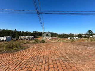 Vista externa de uma área pavimentada com terra e vegetação ao fundo.