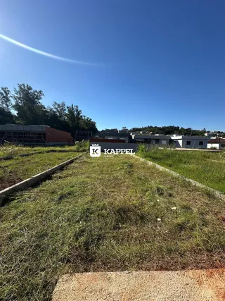 Vista externa de um terreno gramado com vegetação ao fundo sob um céu azul.