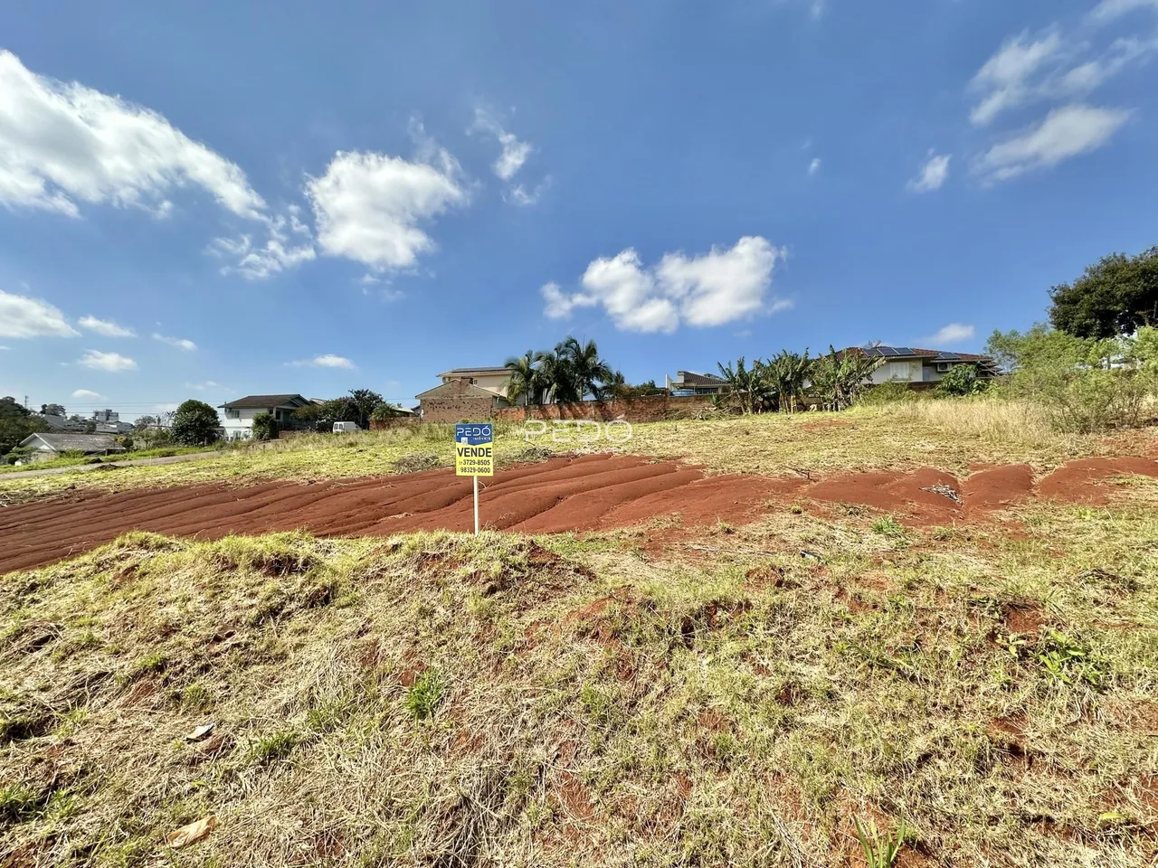 Vista aérea de terreno com vegetação seca e casas ao fundo.
