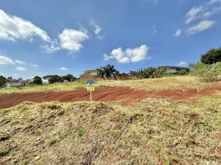 Vista aérea de terreno com vegetação seca e casas ao fundo.