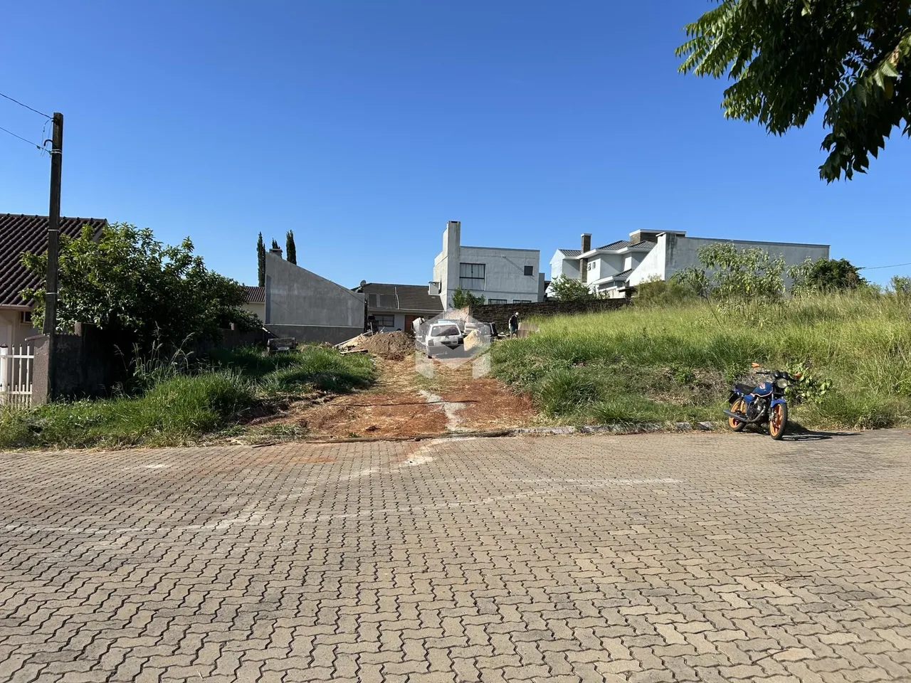 Vista externa de uma propriedade com vegetação e construções ao fundo.