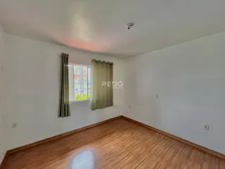 A sala apresenta piso de madeira e uma janela com cortinas.