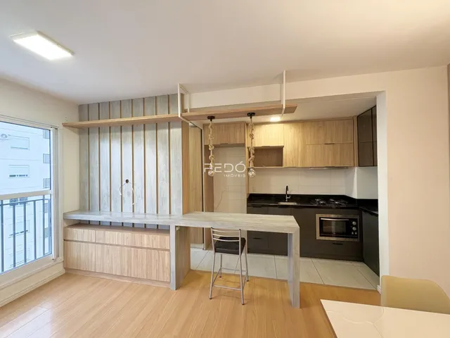 Interior de uma sala de estar com piso de madeira e cozinha integrada.