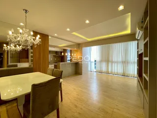 Sala de jantar com piso de madeira clara e grandes janelas.