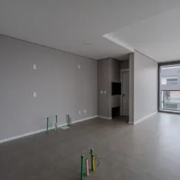 Foto de um ambiente interno vazio com paredes brancas e piso cinza.