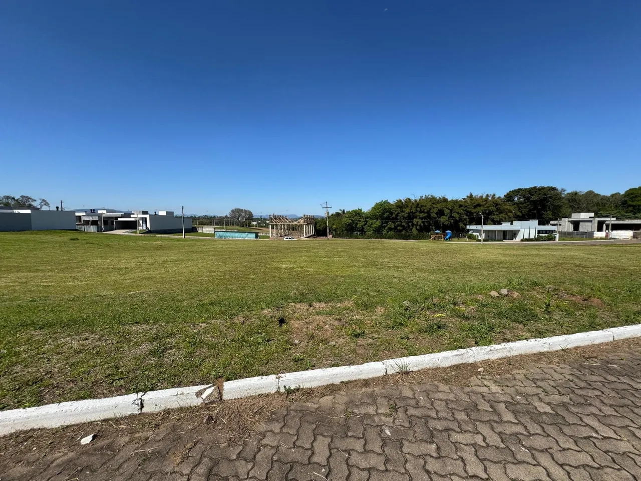 Vista externa de um terreno gramado com construções ao fundo sob um céu azul.