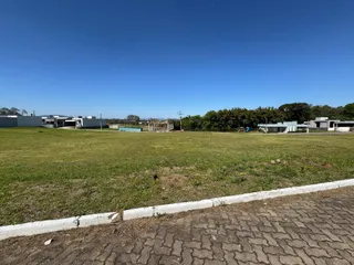 Vista externa de um terreno gramado com construções ao fundo sob um céu azul.