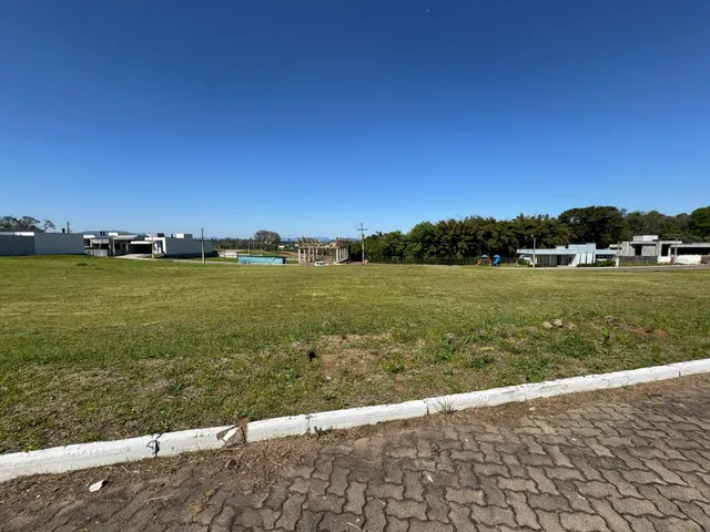 Vista externa de um terreno gramado com construções ao fundo sob um céu azul.