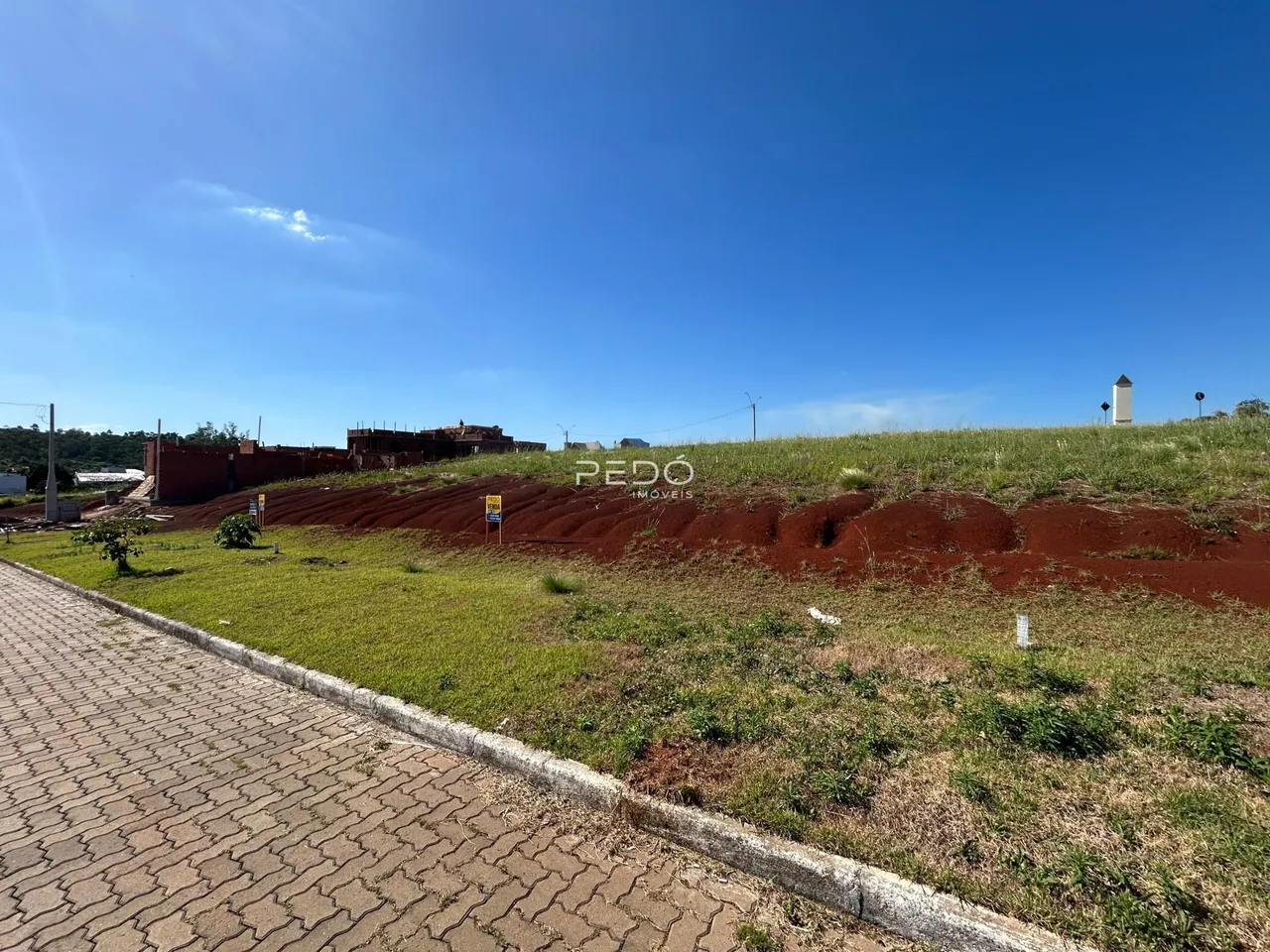 Vista externa de um terreno com grama e uma cerca de tijolos no fundo.