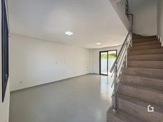 Vista interna de um ambiente amplo com paredes brancas e escadaria de madeira.