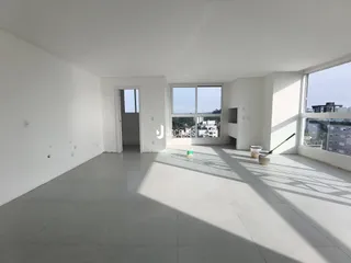 Interior de uma sala ampla com paredes brancas e piso claro.
