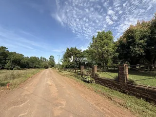 Uma estrada de terra se estende por uma área com cerca e vegetação.