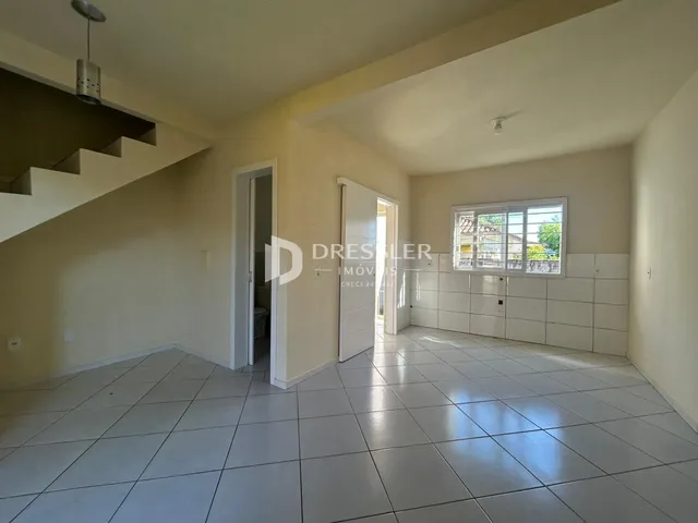 Interior de uma sala com piso de cerâmica e escadaria em um imóvel no Brasil.
