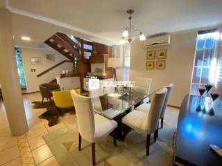 Uma sala de jantar com mesa de vidro e cadeiras brancas é visível no interior da residência.