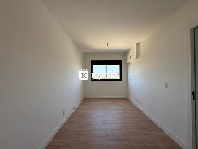 Corredor longo com piso de madeira e janela no final da sala.