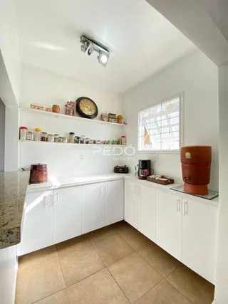 Vista interna de uma cozinha com armários brancos e piso de cerâmica.