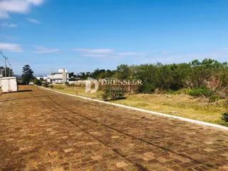 Vista externa de uma área de terreno com vegetação e estruturas ao fundo.