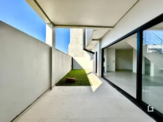 Vista de uma área externa com piso de concreto e jardim lateral em uma residência.