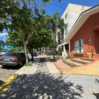 Fachada de uma residência em Lajeado, Brasil, com árvores e carros estacionados na rua.