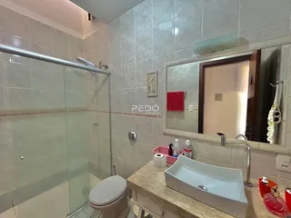 Foto interna de um banheiro com box de vidro e azulejos claros.