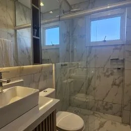 Banheiro com revestimento de mármore claro e bancada branca.