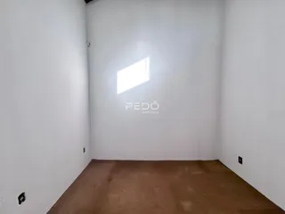 Imagem de um cômodo vazio com paredes brancas e piso de terra.