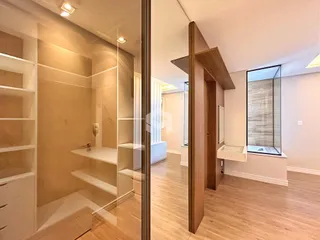 Vista interna de um apartamento moderno com piso de madeira clara e divisória de vidro.