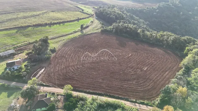 Vista aérea de um campo de terra arada cercado por vegetação e colinas.