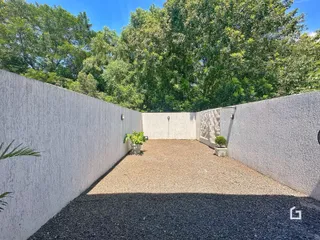 Vista externa de um pátio cercado por paredes brancas e cascalho.