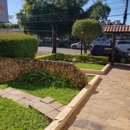 Vista externa do jardim com muro de pedra e caminho pavimentado.