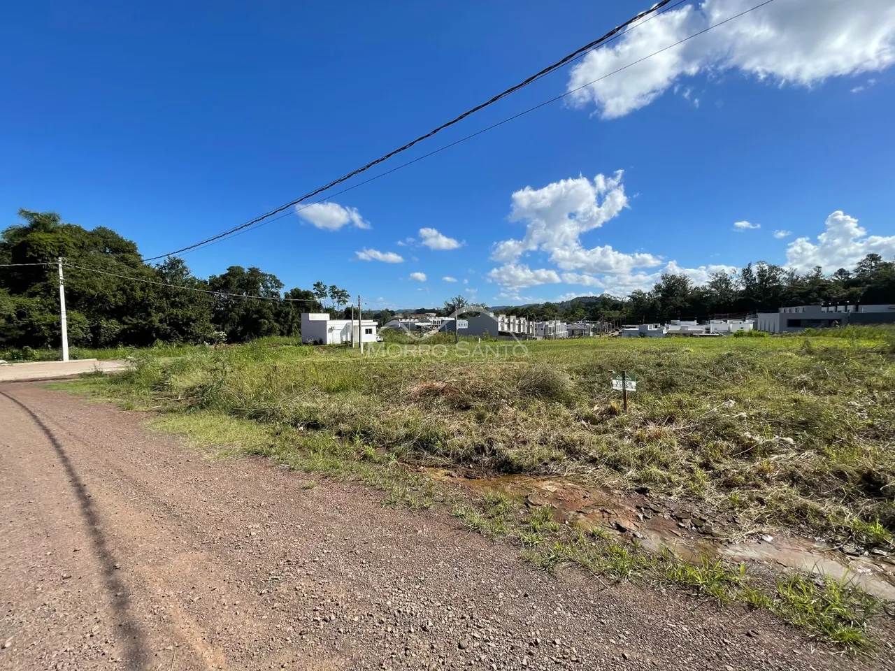 Vista externa de uma área com vegetação e construções ao fundo.