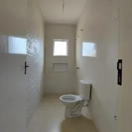 Corredor interno com paredes brancas e um vaso sanitário.