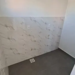 Parede interna com revestimento de mármore claro e piso de cor cinza escura.