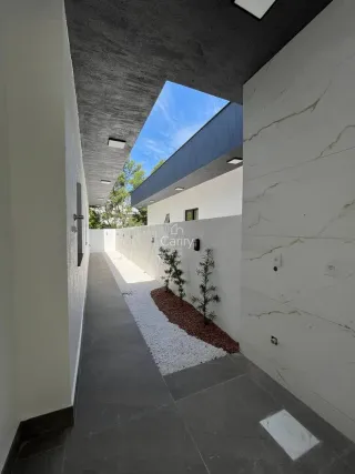 Vista externa de um corredor com piso escuro e parede branca.