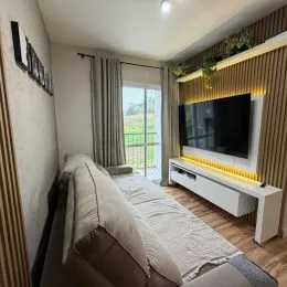 Sala de estar com televisão montada na parede e cortinas claras.