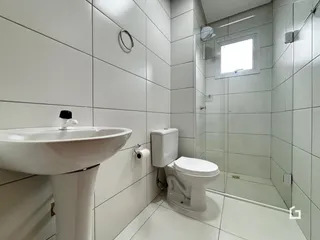 Banheiro com revestimento cerâmico branco e box de vidro.
