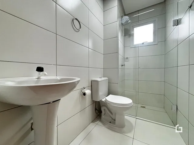 Banheiro com revestimento cerâmico branco e box de vidro.