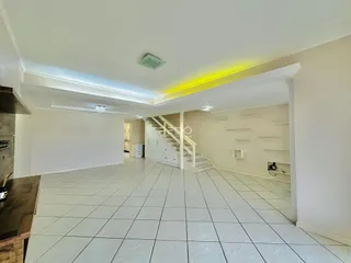 Interior de uma sala ampla com piso de cerâmica e escadaria branca.