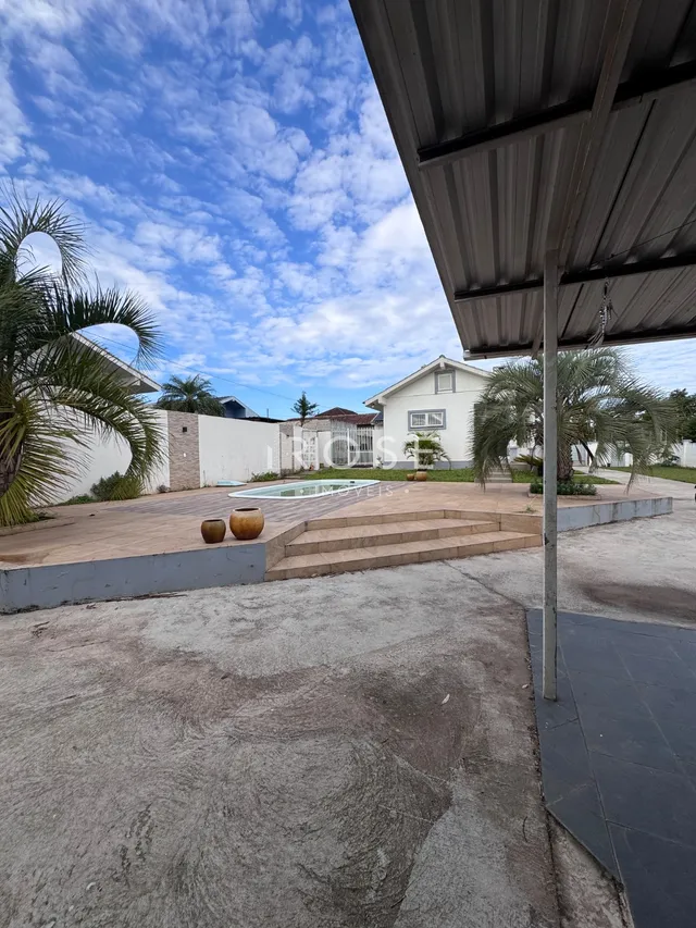 Área externa com piso de concreto e jardim ao lado de uma parede branca.
