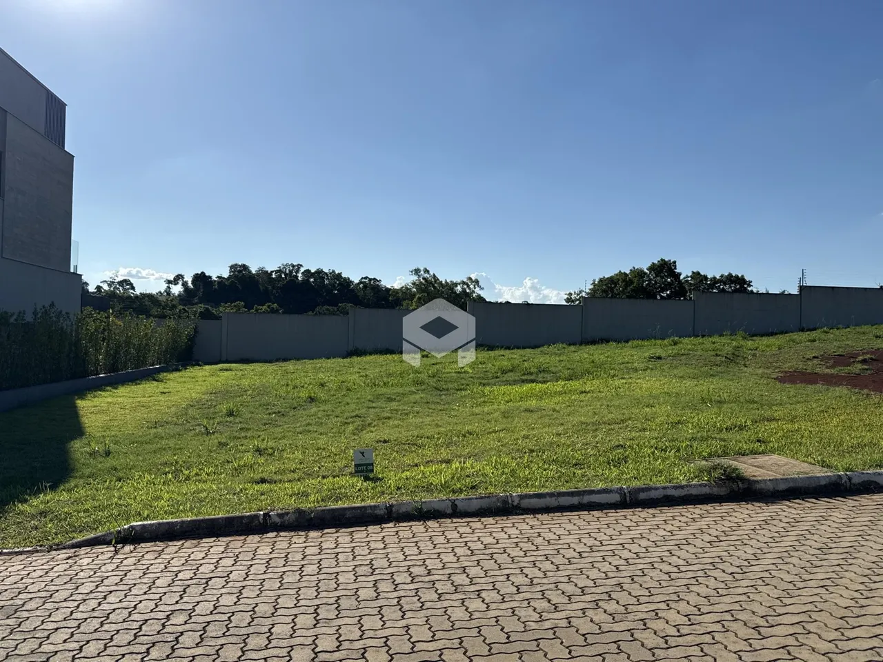 Vista externa de um terreno com gramado e muro de vedação.