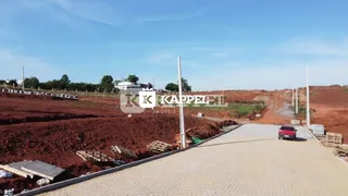 Vista de um terreno aberto com solo avermelhado e área pavimentada.
