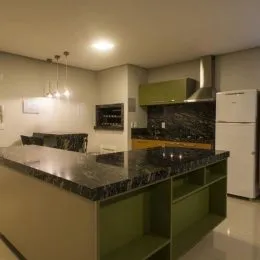Cozinha com bancada escura e armários verdes.