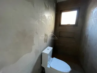 Banheiro com vaso sanitário branco em um corredor.