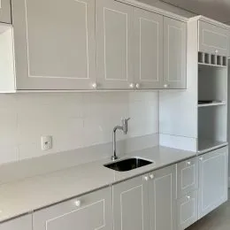 Cozinha branca com armários superiores e bancada clara.