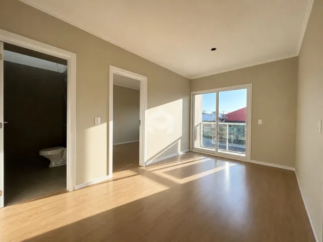 Vista interna de uma sala com piso de madeira clara e paredes bege.