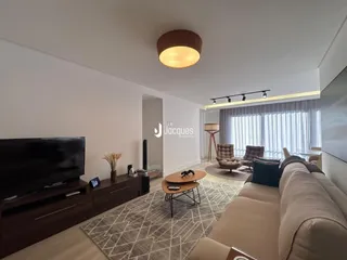 Sala de estar moderna com sofá e televisão em um ambiente claro.