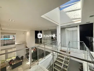 Vista de um corredor com escadaria de vidro e teto de claraboia em um apartamento.