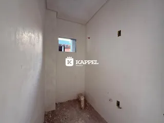 Corredor estreito com paredes brancas e piso cru, mostrando o interior da residência.