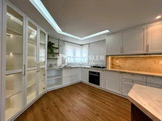 Vista interna de uma cozinha moderna com armários brancos e piso de madeira.